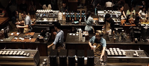 Vue plongeante sur une équipe de baristas préparant et servant des cafés derrière le comptoir d’un café très fréquenté.